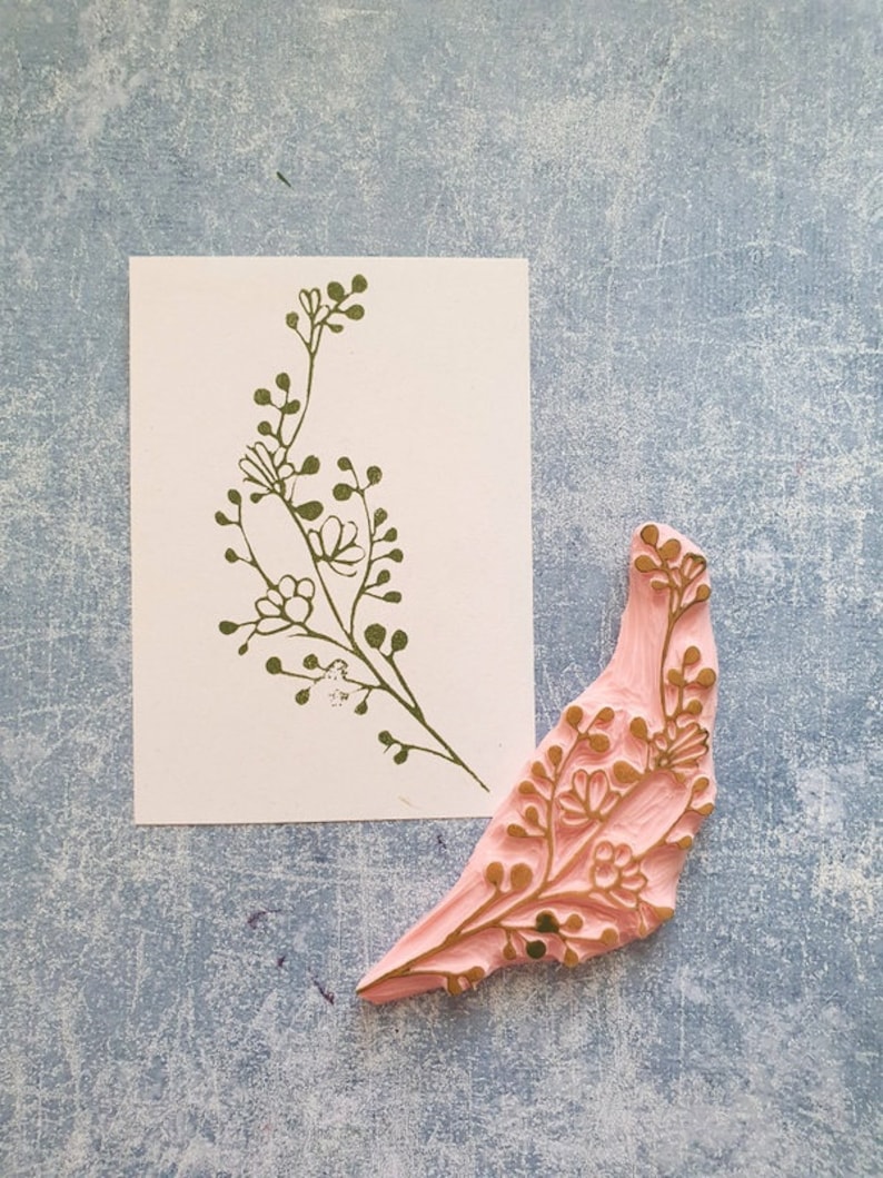 May include: A pink rubber stamp with a gold floral design. The stamp is shaped like a leaf and has a detailed floral pattern.