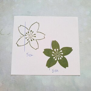 Peut inclure: Deux d&eacute;coupes en papier de fleurs de cerisier, une blanche et une verte, avec des dimensions de 5 cm et 1,5 cm.