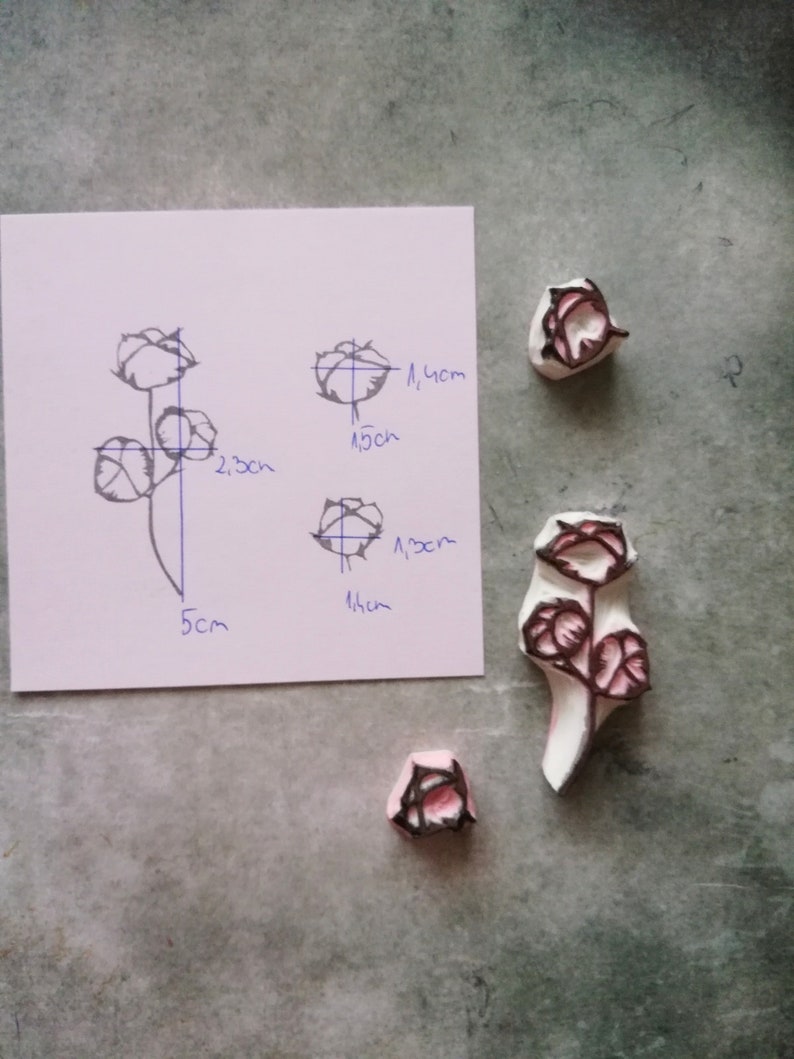 May include: A collection of handmade rose stamps and a sketch. The stamps are white with pink and black rose details. The sketch on a white paper shows a rose design with measurements in centimeters.