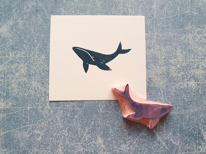 May include: A black whale silhouette rubber stamp on a white card with a pink whale rubber stamp on a gray surface.