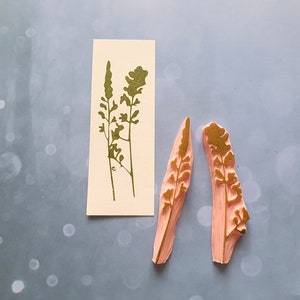 May include: Two pink rubber stamps with gold leaf designs of stylised floral sprigs. The stamps are on a light blue background.