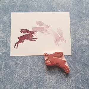 May include: A set of four rubber stamps featuring a design of three hares running. The stamps are pink and red and are on a light blue background.