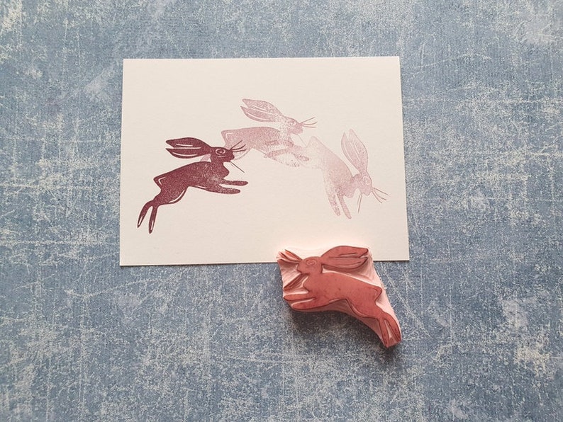 May include: A set of four rubber stamps featuring a design of three hares running. The stamps are pink and red and are on a light blue background.