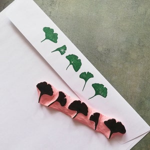 May include: A set of five pink rubber stamps with black ginkgo leaf designs. The stamps are arranged in a row on a white envelope.