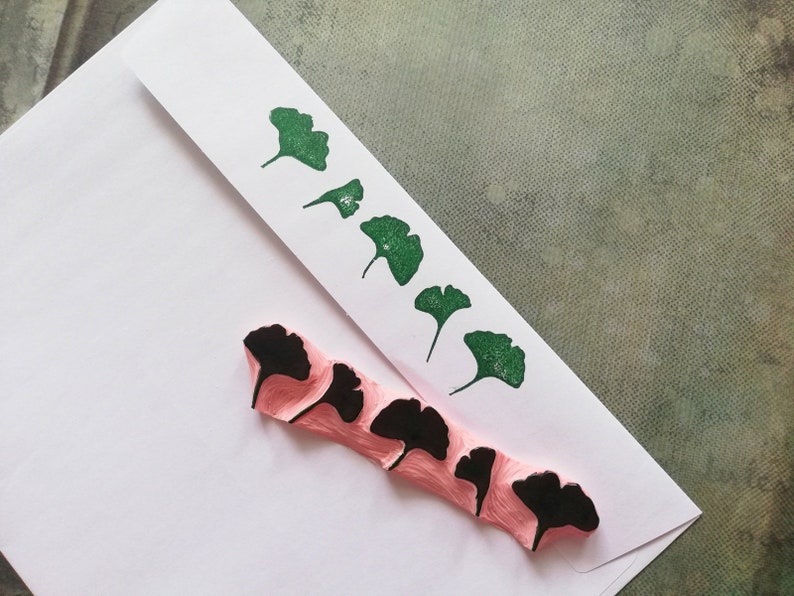 May include: A set of five pink rubber stamps with black ginkgo leaf designs. The stamps are arranged in a row on a white envelope.