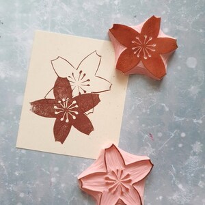 Peut inclure: Trois tampons en bois avec un motif de fleur de cerisier. Deux tampons sont bruns et un est rose.
