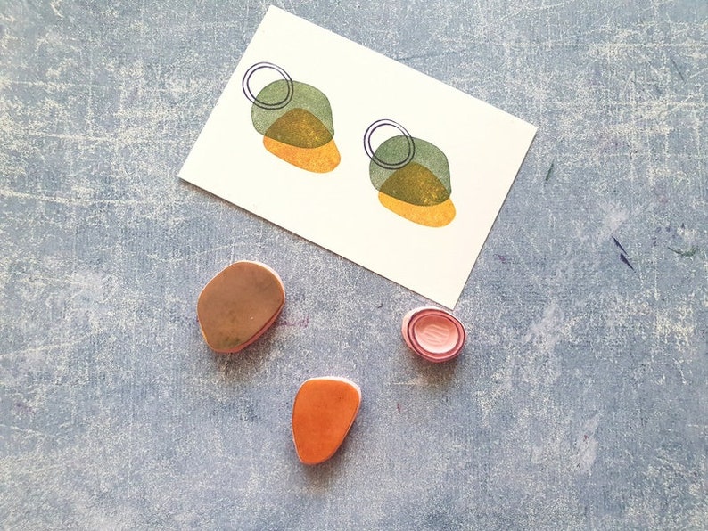May include: A set of four polymer clay earrings in shades of green, orange, and pink. The earrings are shaped like abstract geometric shapes with a circle design.