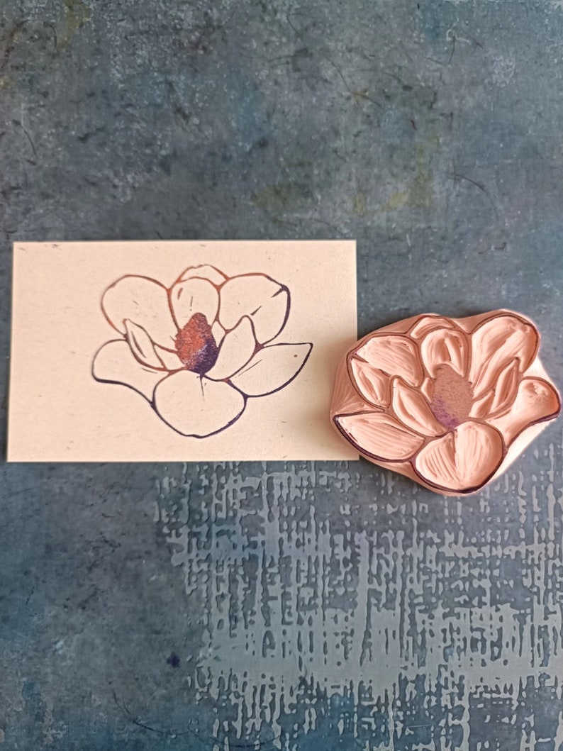 Może przedstawiać: R&oacute;żowa gumowa pieczątka z detalicznym wzorem magnolii. Pieczątka służy do tworzenia odcisku kwiatu na papierze.