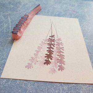 May include: A wooden stamp with a design of a bunch of lavender flowers. The stamp is pink and the design is brown. The stamp is on a piece of paper with a pink impression of the design.