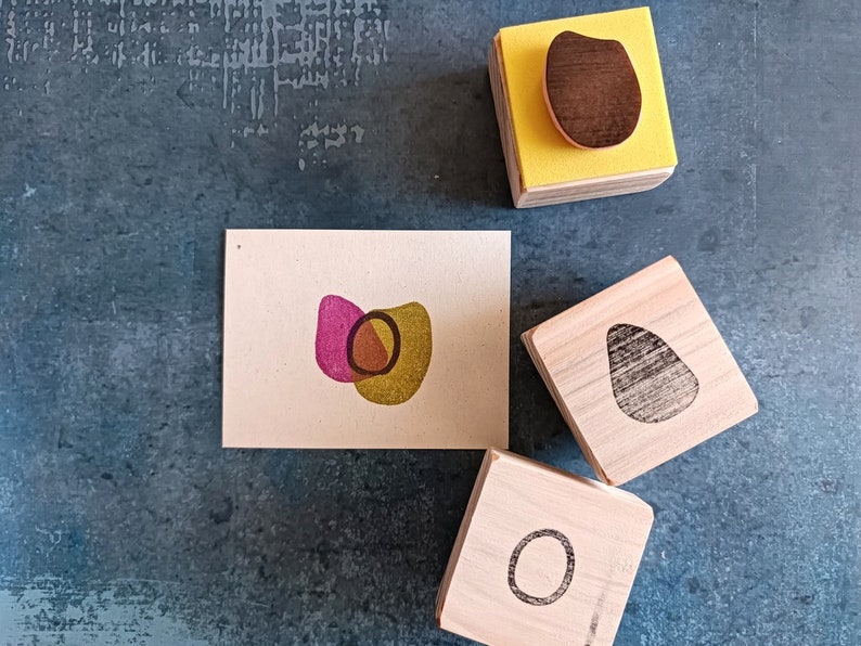 May include: Three wooden blocks with different shapes carved into them. The shapes are a circle, an oval, and a teardrop. The blocks are all natural wood color and have a smooth finish.