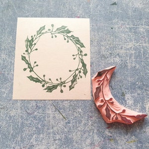 Könnte beinhalten: Ein Holz-Stempel mit einem Design aus einer Stechpalmenkrone. Der Stempel ist rosa und hat eine grüne Stechpalmenkrone mit roten Beeren.