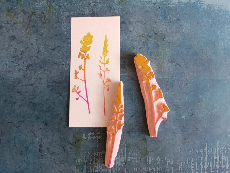 May include: Two wooden stamps featuring a floral design. The stamps are carved with a delicate pattern of leaves and stems. The stamps are painted in shades of orange and yellow.