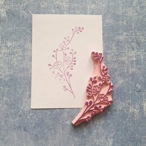 May include: A pink wooden stamp with a floral design. The stamp is carved with a delicate pattern of leaves and flowers. The stamp is used to create a floral print on paper.