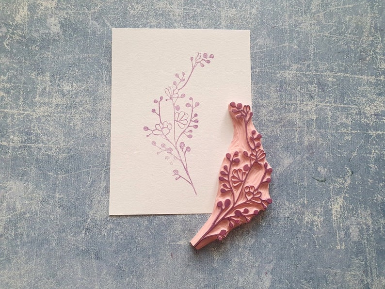 May include: A pink wooden stamp with a floral design. The stamp is carved with a delicate pattern of leaves and flowers. The stamp is used to create a floral print on paper.
