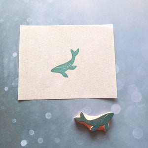 May include: A green whale rubber stamp on a white card. The stamp is also shown separately on a light blue background.