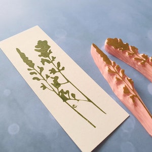May include: Two pink rubber stamps with a gold floral design. The stamps are used to create a floral pattern on paper.