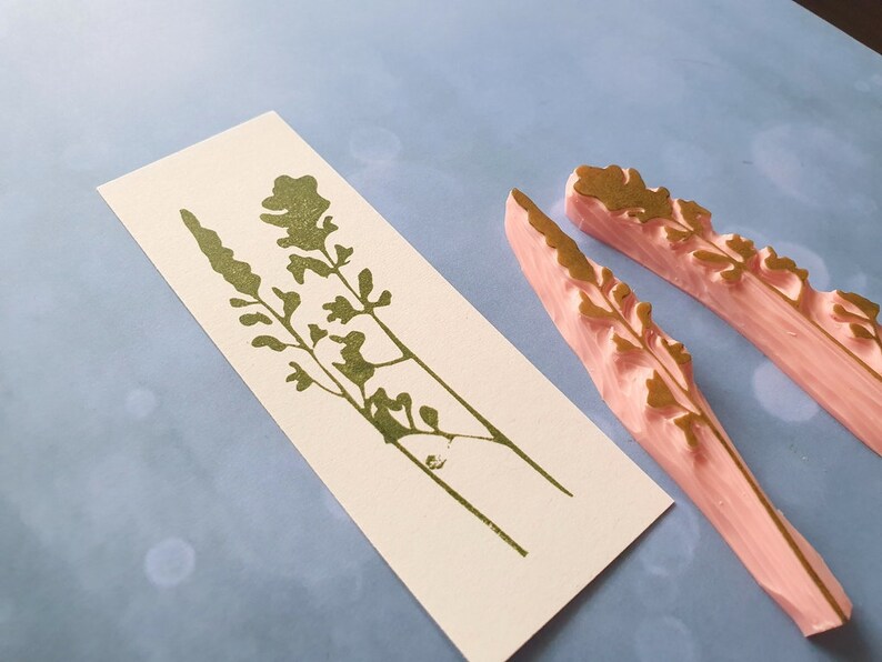 May include: Two pink rubber stamps with a gold floral design. The stamps are used to create a floral pattern on paper.