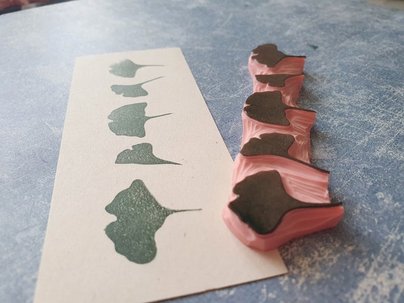 May include: A set of six ginkgo leaf stamps, with a pink rubber base and black ink. The stamps are arranged in a row, with the largest leaf at the top and the smallest leaf at the bottom.