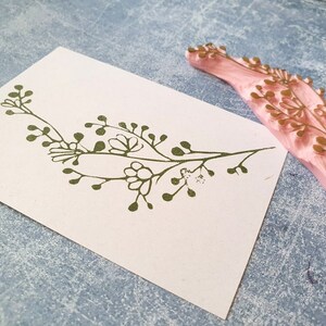 May include: A green floral design stamp with a pink rubber base. The stamp is used to create a floral design on paper.