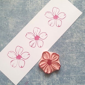Pode incluir: Um carimbo de borracha rosa com um desenho de flor. O carimbo est&aacute; em um cart&atilde;o branco com tr&ecirc;s impress&otilde;es de flores rosas.
