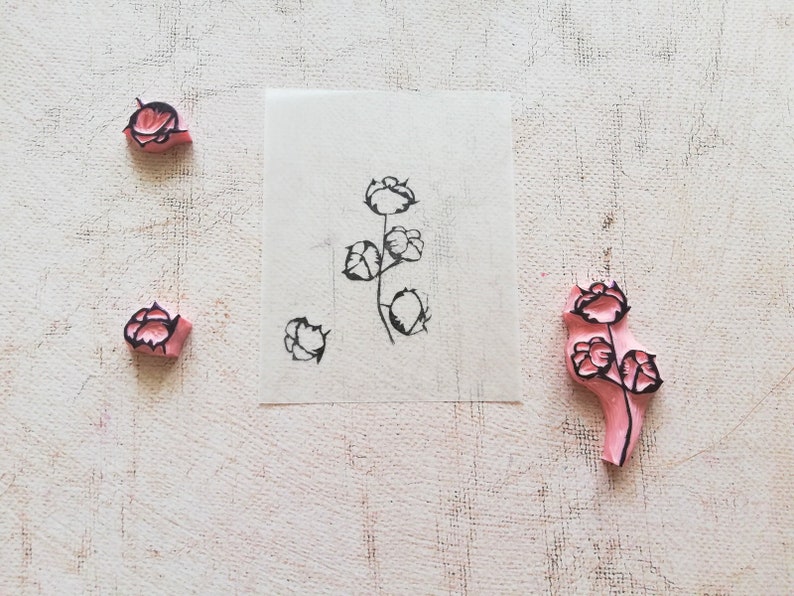 May include: A collection of floral stamps and a stamped image on paper. The stamps are pink with black floral designs. The stamped image shows a stem with several flowers. The background is a textured, off-white surface.
