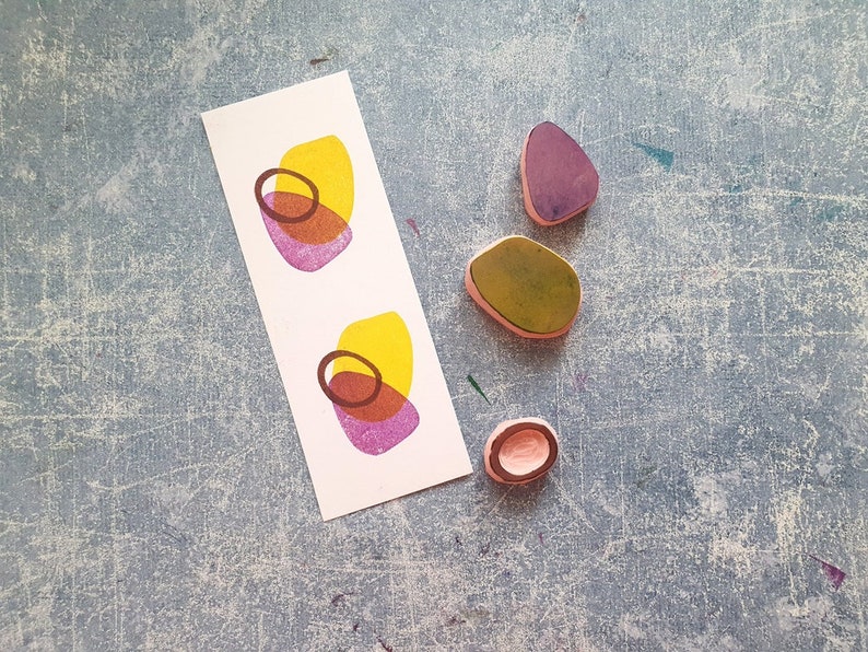 May include: Four rubber stamps with abstract shapes. Two stamps are yellow, pink, and brown. One stamp is green. One stamp is purple.