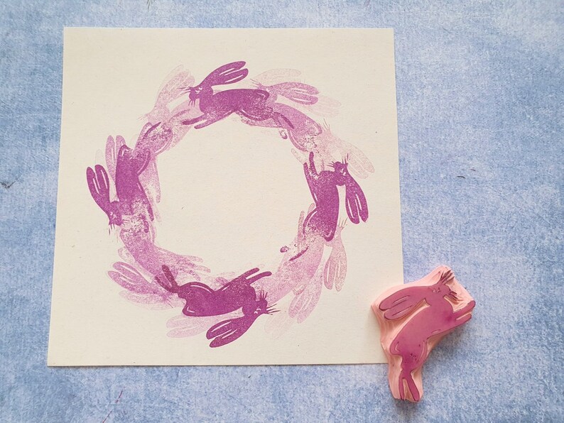 May include: A pink rubber stamp with a design of a circle of bunnies. The stamp is on a white background.