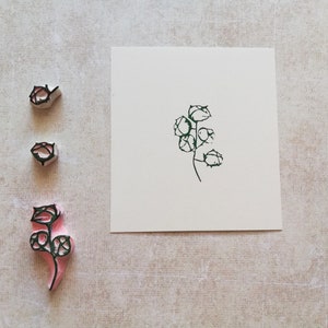 May include: A set of three floral stamps with a botanical design. The stamps are in various stages of completion, with a green ink impression on a white card. The stamps are pink and gray.