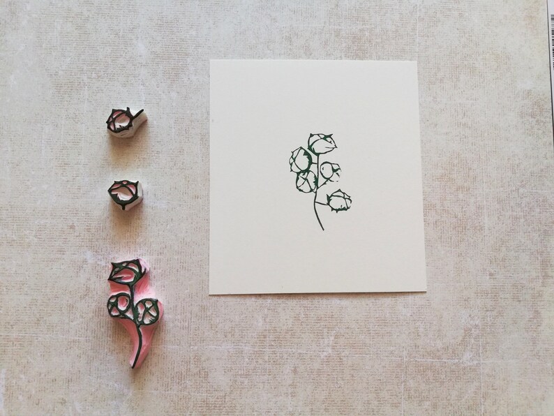 May include: A set of three floral stamps with a botanical design. The stamps are in various stages of completion, with a green ink impression on a white card. The stamps are pink and gray.