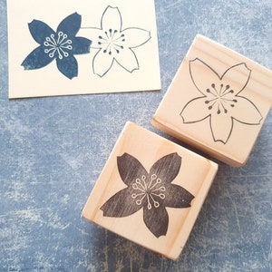 Peut inclure: Deux blocs de bois avec un motif de fleur de cerisier grav&eacute;. Un bloc a une fleur de cerisier noire et l'autre a une fleur de cerisier blanche.