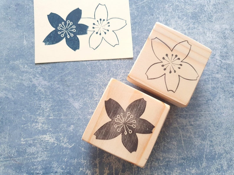 Peut inclure: Deux blocs de bois avec un motif de fleur de cerisier grav&eacute;. Un bloc a une fleur de cerisier noire et l'autre a une fleur de cerisier blanche.