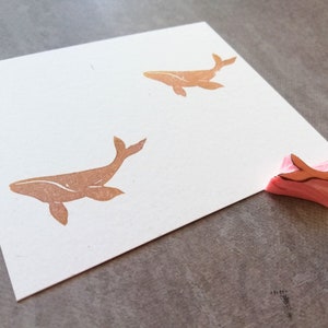 May include: Two brown whale stamps on a white card with a pink rubber whale stamp on a gray surface.