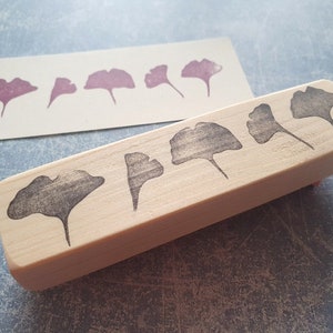 May include: A wooden block stamp with five ginkgo leaf designs carved into the surface. The leaves are arranged in a row, with the largest leaf at the center. The stamp is made of light-colored wood and has a natural finish.