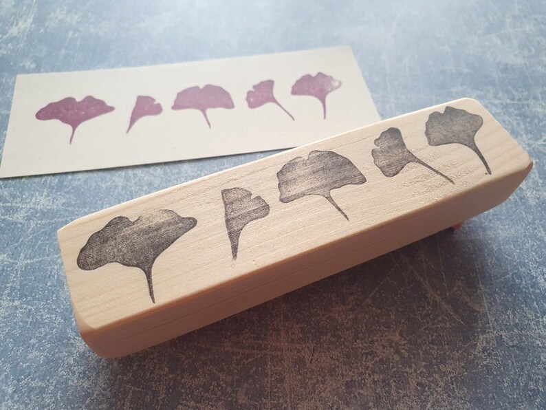 May include: A wooden block stamp with five ginkgo leaf designs carved into the surface. The leaves are arranged in a row, with the largest leaf at the center. The stamp is made of light-colored wood and has a natural finish.
