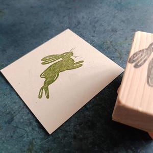 May include: A wooden stamp with a green rabbit design. The rabbit is in a jumping pose with its ears up.