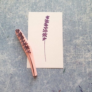 May include: A wooden stamp with a purple lavender design. The stamp is on a white card with a purple lavender design printed on it.
