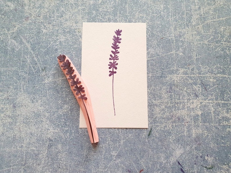May include: A wooden stamp with a purple lavender design. The stamp is on a white card with a purple lavender design printed on it.