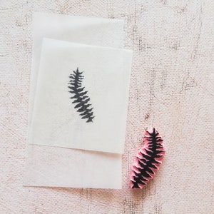 May include: A black fern leaf design rubber stamp on a white background. The stamp is pink and has a black fern leaf design.