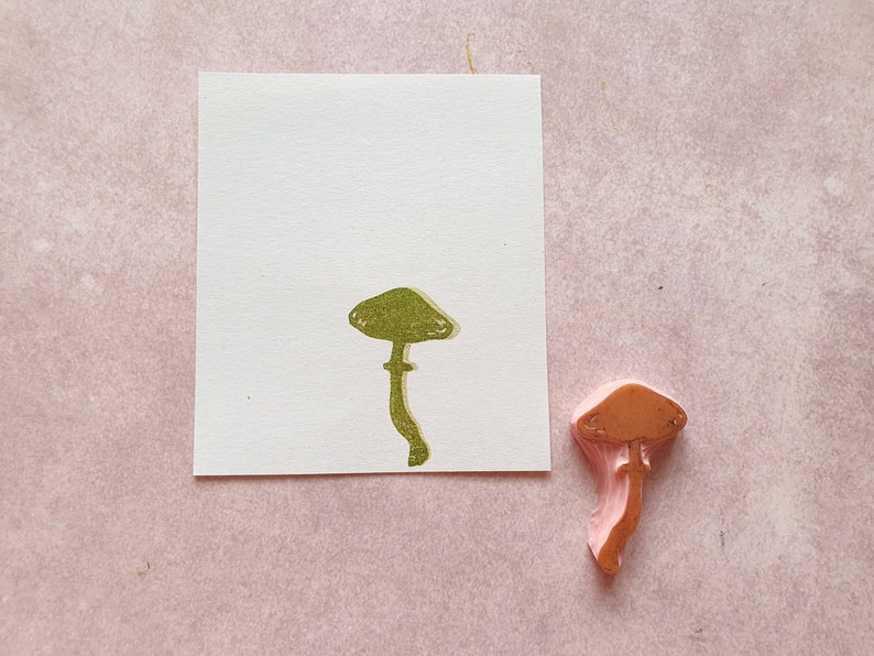 K&ouml;nnte beinhalten: Nahaufnahme eines rosa Gummistempels in Form eines Pilzes. Der Stempel befindet sich auf einer wei&szlig;en Karte mit einem gr&uuml;nen Pilzabdruck.