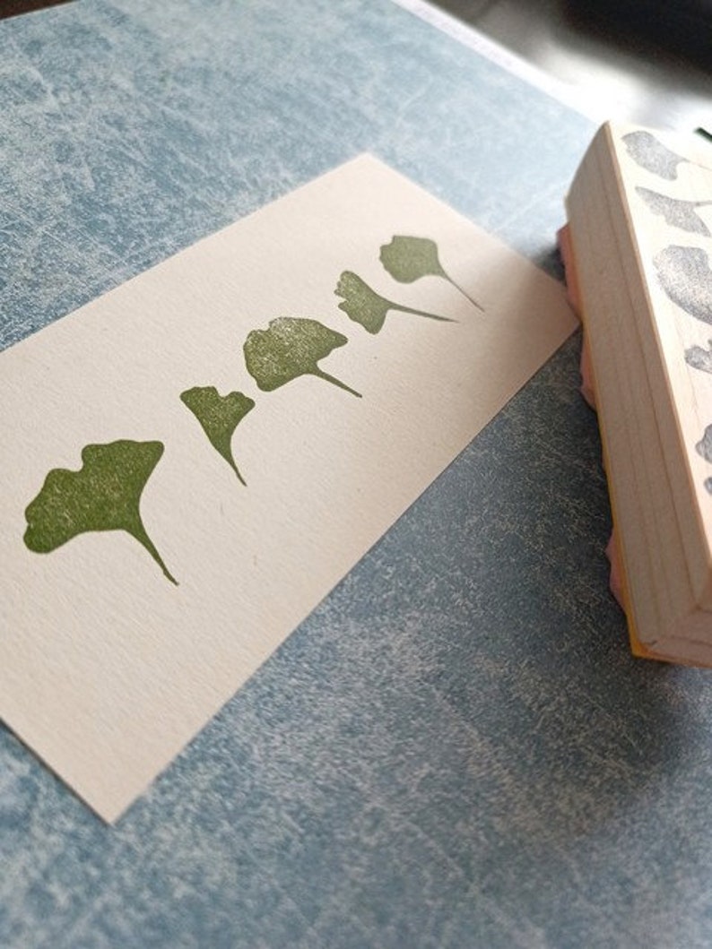 May include: A set of five green rubber stamps featuring different ginkgo leaf designs. The stamps are mounted on wooden blocks.