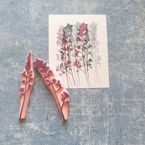 May include: Two wooden stamps with a floral design. The stamps are pink with a dark red floral pattern. The stamps are on a grey textured surface.