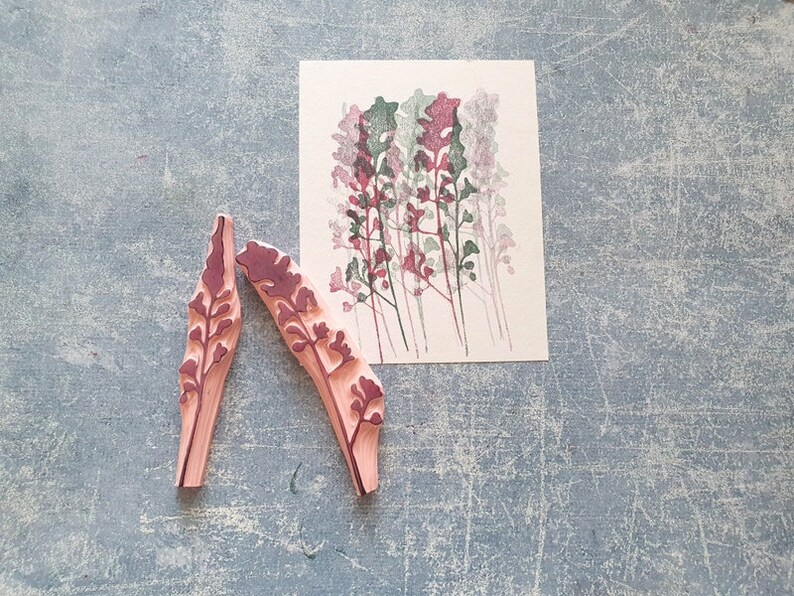 May include: Two wooden stamps with a floral design. The stamps are pink with a dark red floral pattern. The stamps are on a grey textured surface.
