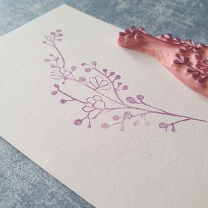 May include: A pink rubber stamp with a floral design. The stamp has been used to create a purple floral design on a white card.