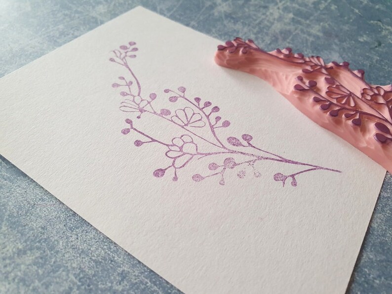 May include: A pink rubber stamp with a floral design. The stamp has been used to create a purple floral design on a white card.