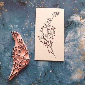 May include: A wooden stamp with a floral design, and a card with a floral design printed on it. The stamp is pink and the card is cream.