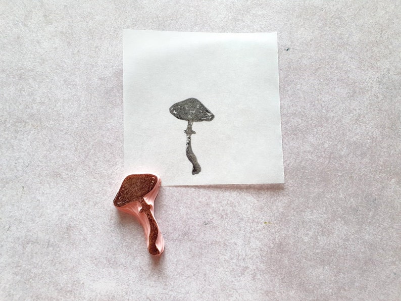 K&ouml;nnte beinhalten: Ein brauner Gummistempel in Form eines Pilzes. Der Stempel wurde verwendet, um einen Abdruck eines Pilzes auf einem wei&szlig;en Blatt Papier zu erstellen.