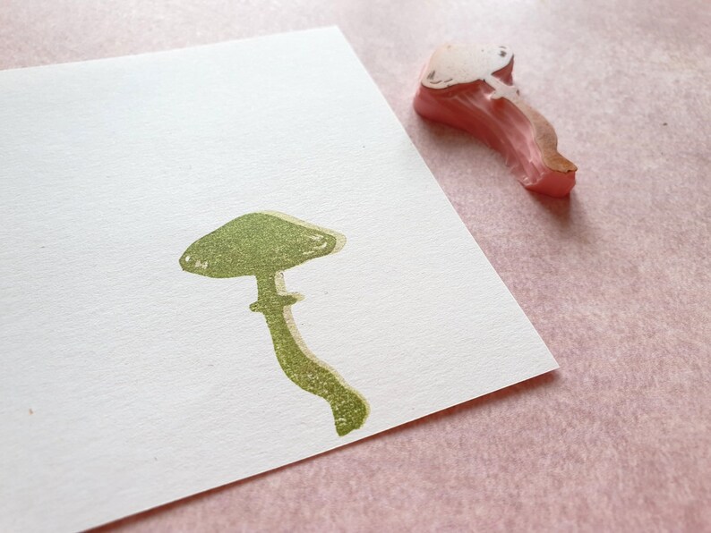 K&ouml;nnte beinhalten: Ein gr&uuml;ner Gummistempel mit einem Pilz mit abgerundetem Hut und Stiel. Der Stempel befindet sich auf einem wei&szlig;en Blatt Papier.