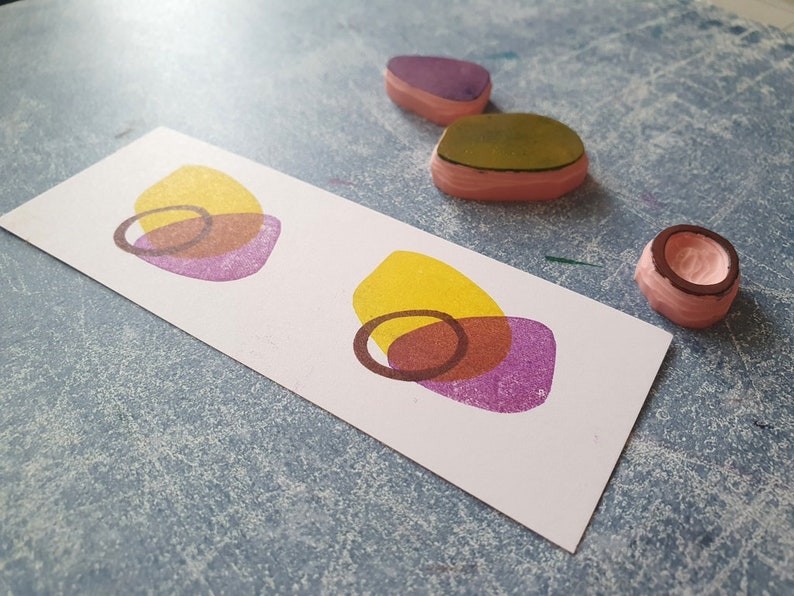 May include: Two sets of overlapping circles in yellow, brown, and purple on a white card. The circles are printed with a rubber stamp.