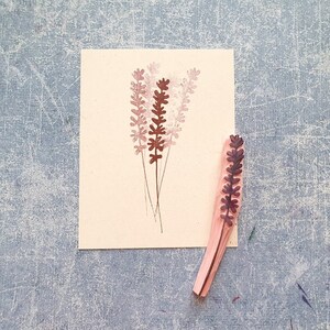 May include: A wooden stamp with a design of a lavender flower. The stamp is brown and pink and is on a white background.