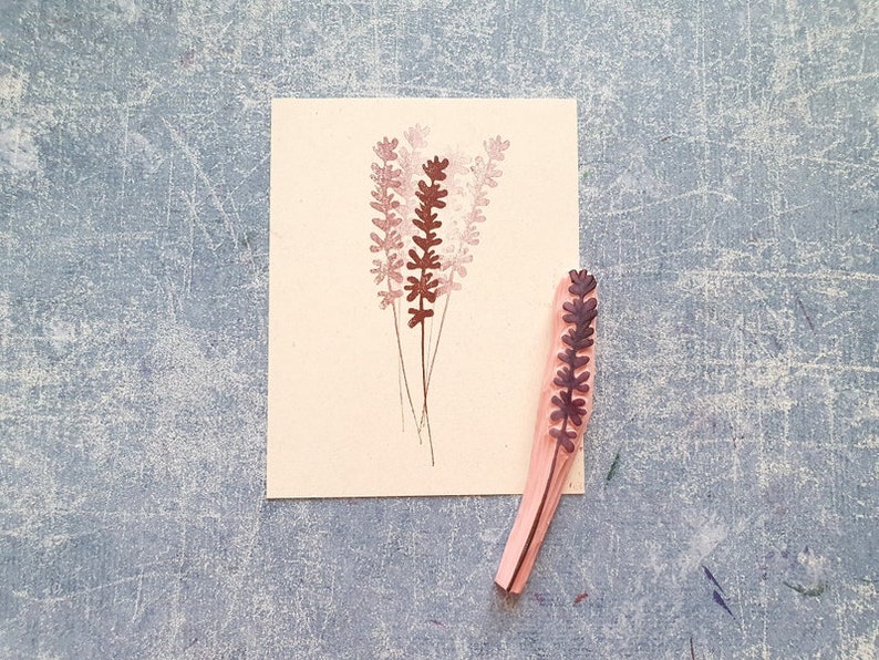 May include: A wooden stamp with a design of a lavender flower. The stamp is brown and pink and is on a white background.